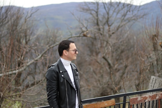 Model wearing a sleek black leather jacket standing against a rugged mountain backdrop.