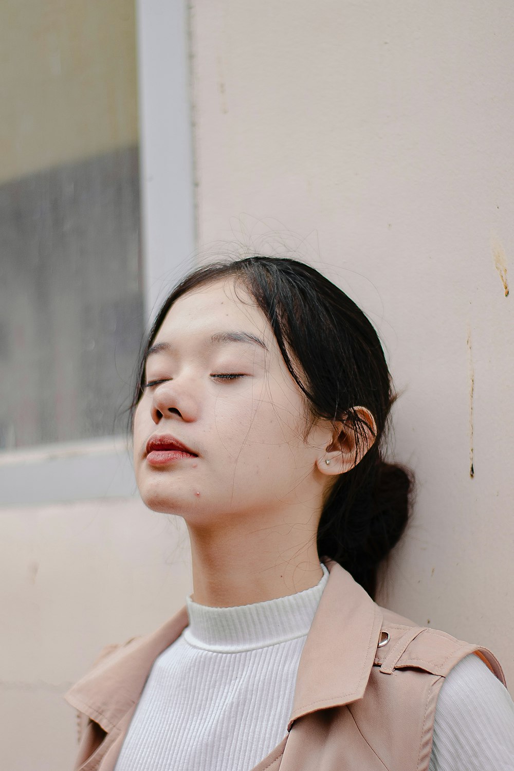 a woman with her eyes closed leaning against a wall