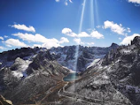 Sunlight illuminating snow-capped peaks reflecting over a serene blue lake in Spiti Valley.