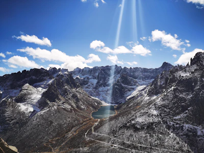 Sunlight illuminating snow-capped peaks reflecting over a serene blue lake in Spiti Valley.