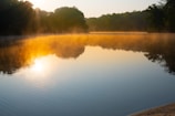 A serene sunrise over a quiet lake with mist rising from the water.
