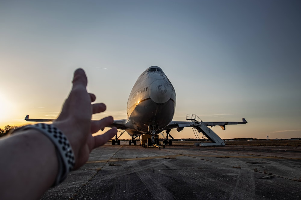 a person's hand pointing at a plane on the tarmac