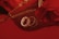 A collection of bracelets, including a pearl bracelet, and gold chain jewelry are arranged on a reflective surface. There is a rose in the image and a zipper that appears to belong to a bag or pouch, all set against a red background.