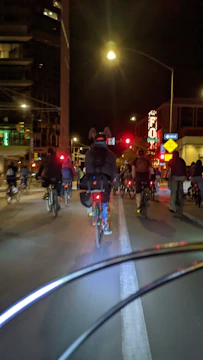 A group of young riders cruising through a busy city road, their bikes lit by neon reflections.