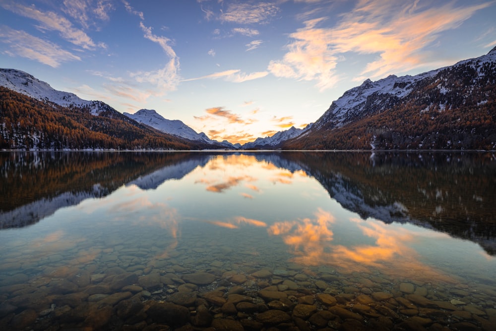 a lake surrounded by mountains under a cloudy sky