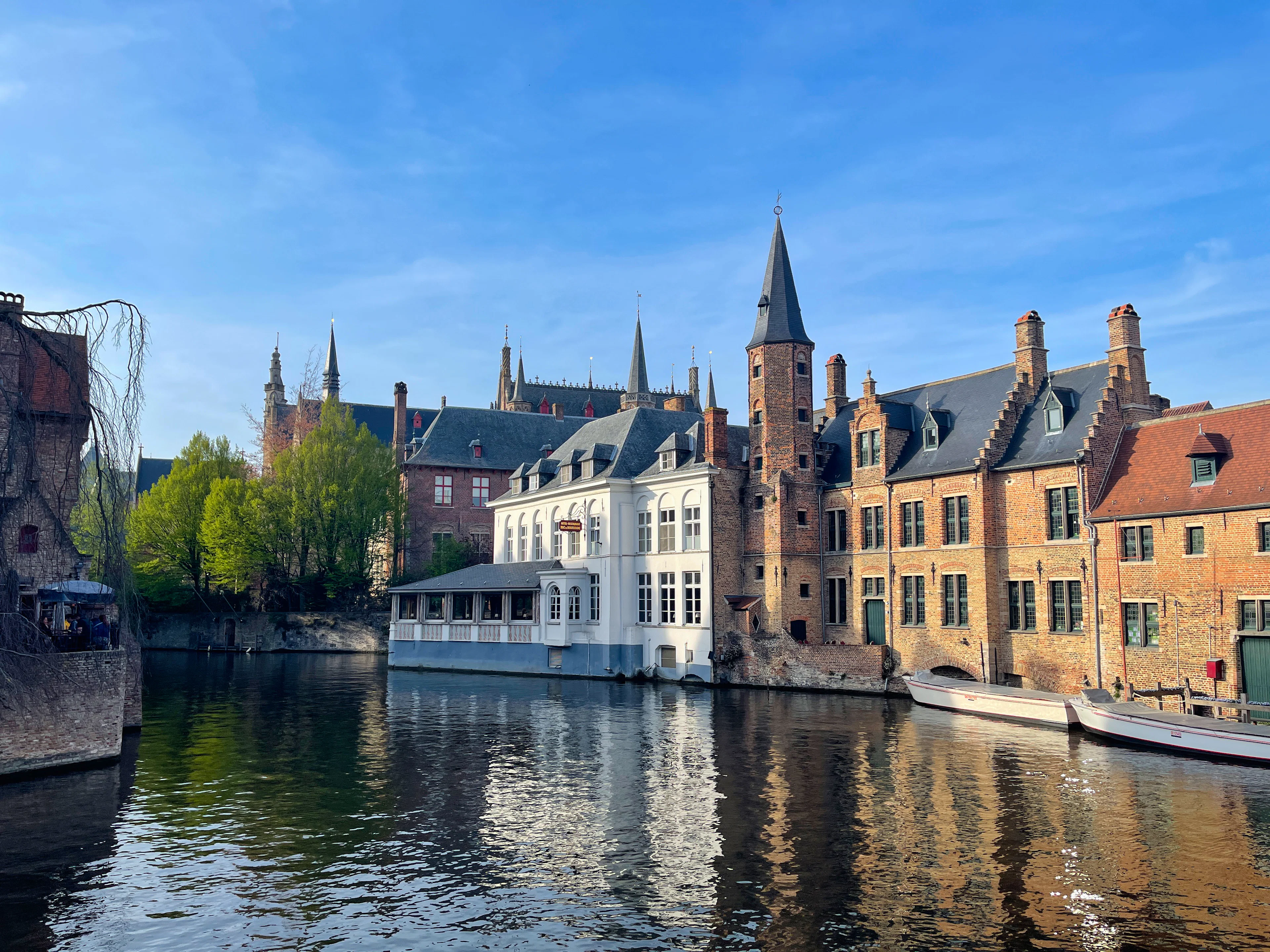 A Bruges canal lined with medieval brick gabled houses beneath a church spire and blue sky