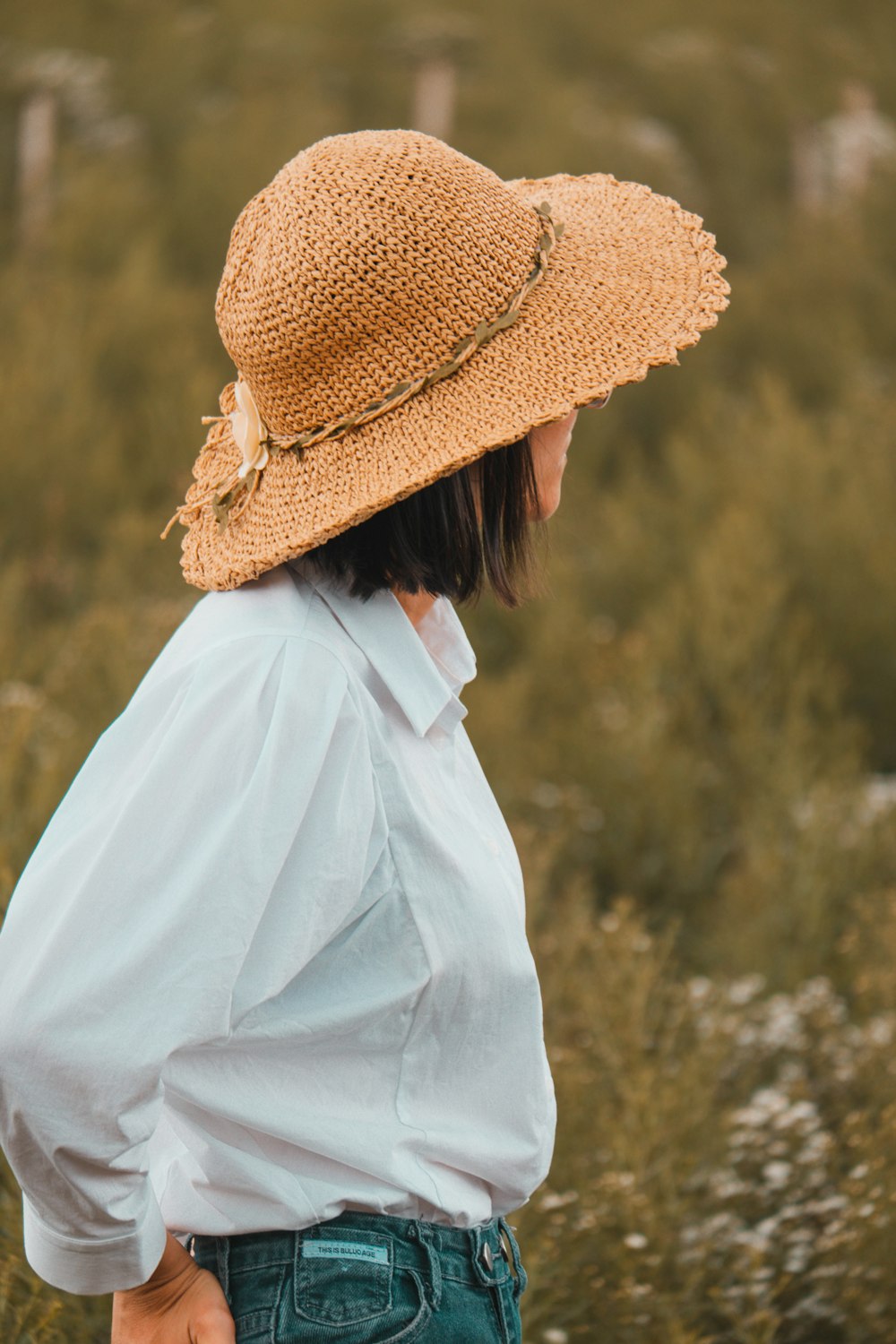 a woman standing in a field wearing a straw hat
