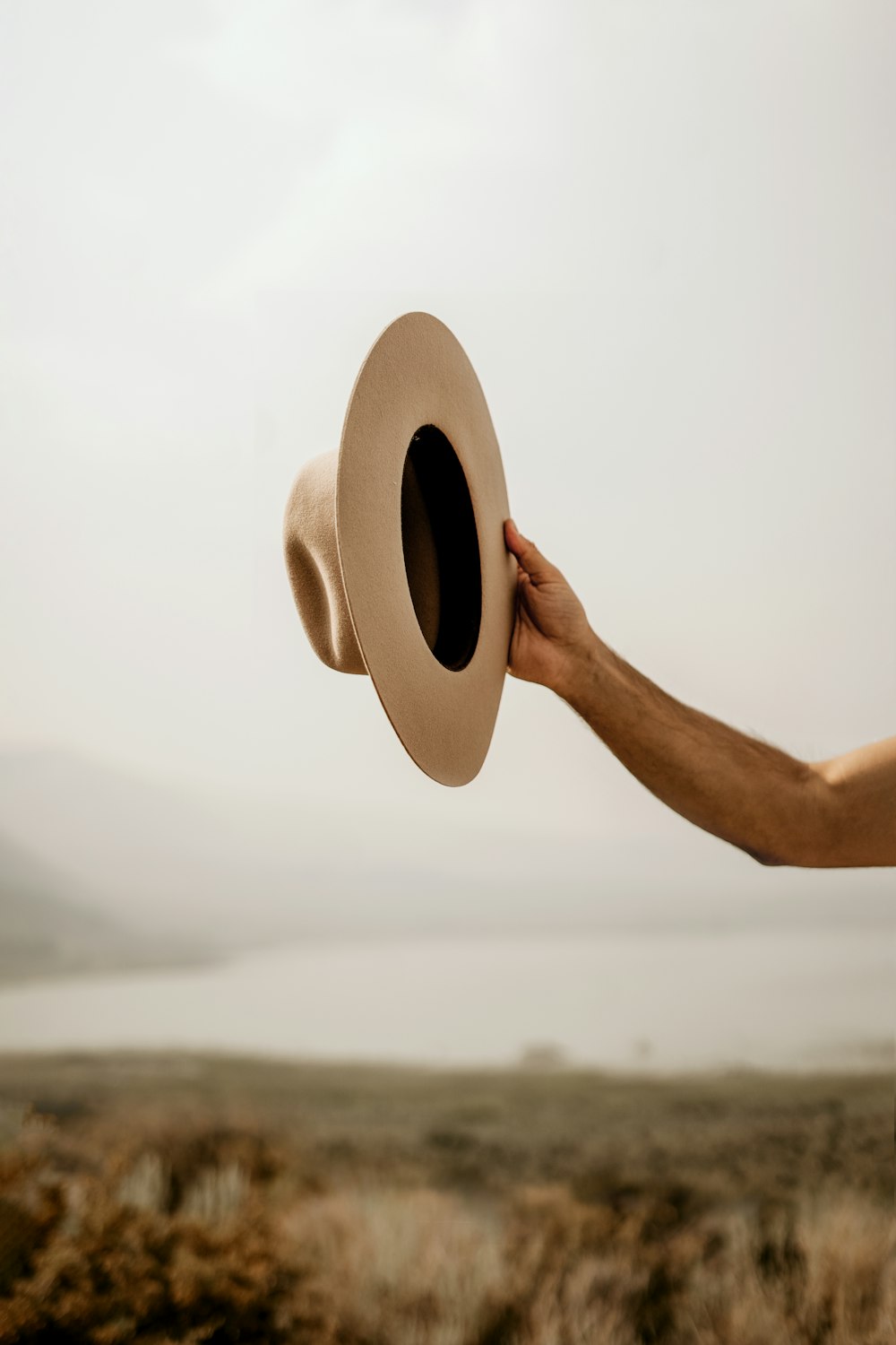 a person holding a hat in front of a body of water