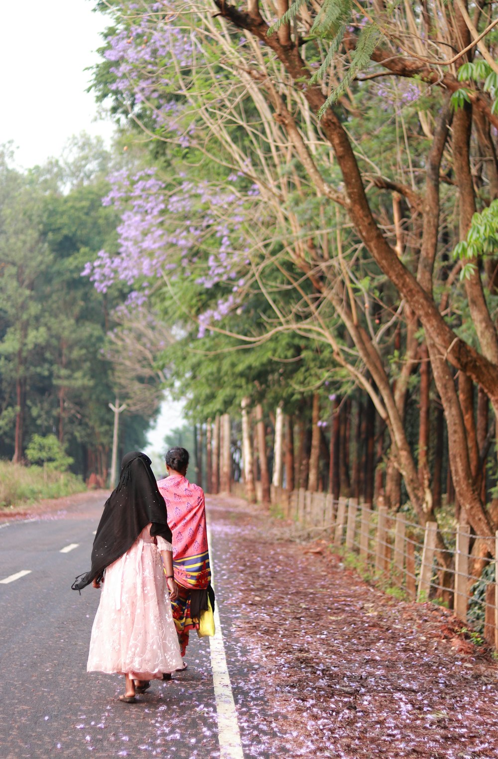 a woman walking down a road with a black umbrella