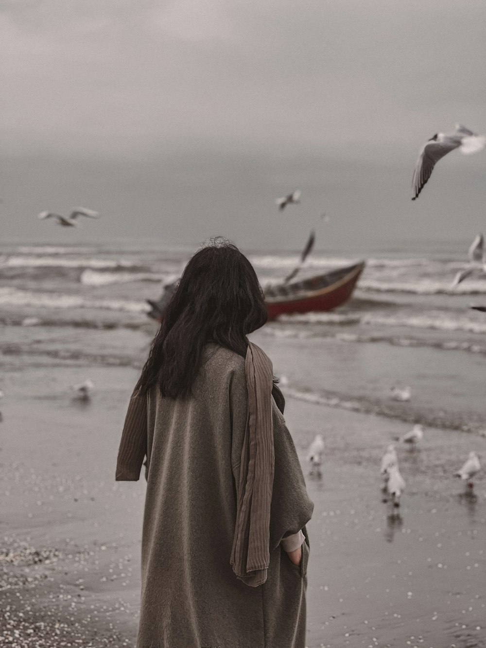 a woman standing on a beach looking at seagulls