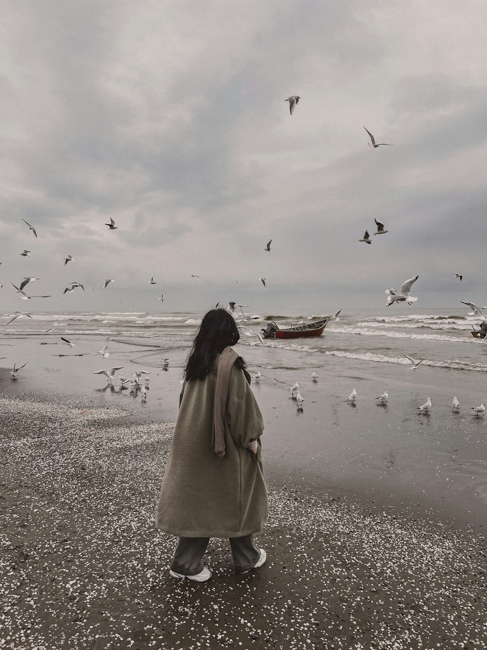 a woman standing on top of a beach next to a flock of birds