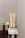 A beige cosmetic tube with gold accents is placed on a metallic stand. The tube features text and branding and appears to be a skincare product. A minimalistic and clean background is used, primarily showcasing the product without distractions.