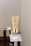 A beige cosmetic tube with gold accents is placed on a metallic stand. The tube features text and branding and appears to be a skincare product. A minimalistic and clean background is used, primarily showcasing the product without distractions.