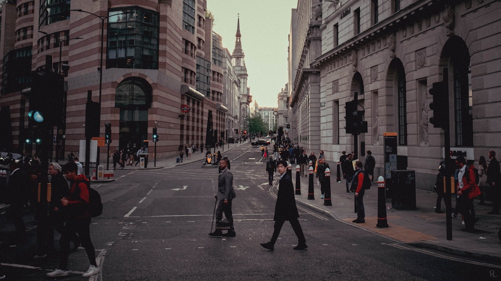 a group of people walking across a street next to tall buildings