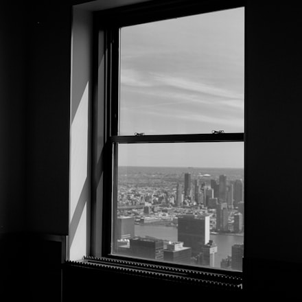 a black and white photo of a window with a view of a city