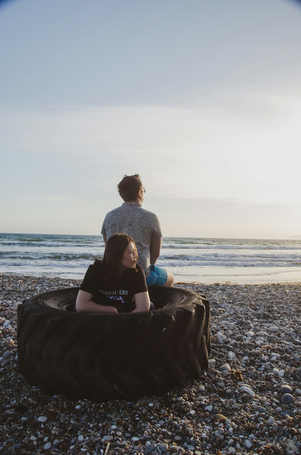 um homem e uma mulher sentados em um pneu na praia