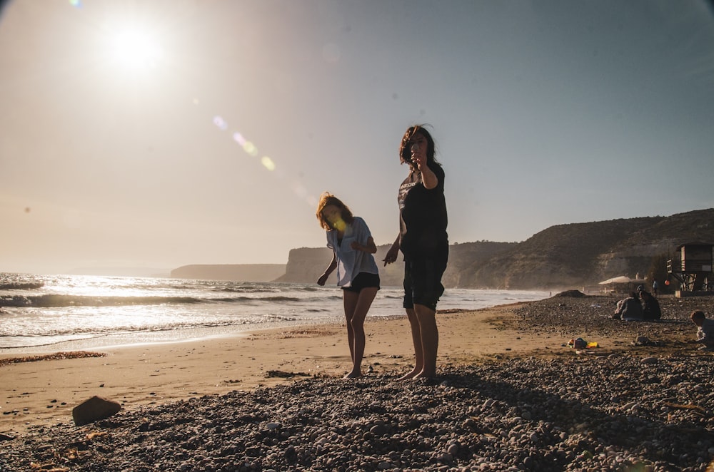 um casal de mulheres em pé no topo de uma praia de areia
