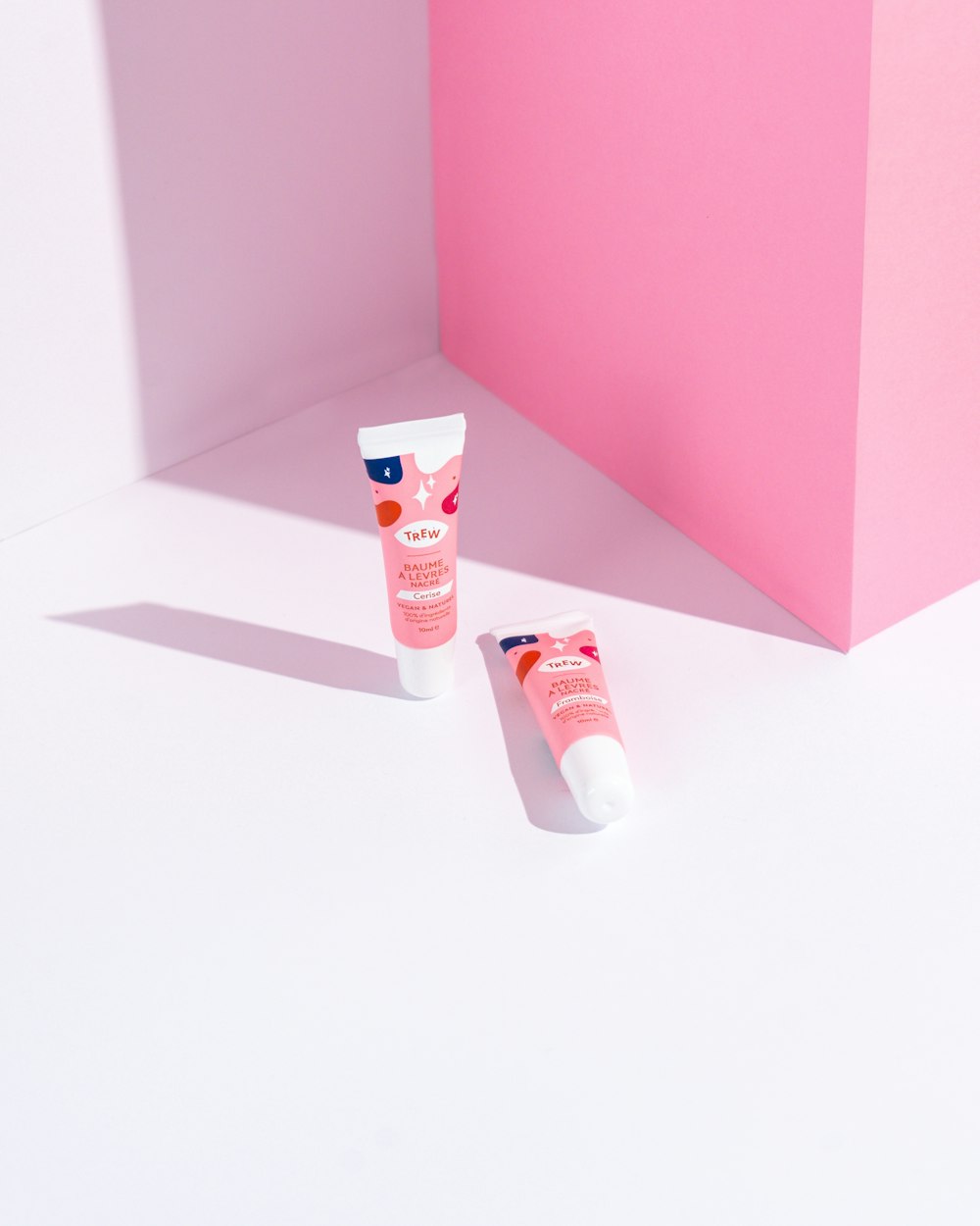 dois tubos de pasta de dente sentados ao lado de uma caixa rosa