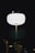 A bright, round street lamp illuminates the surrounding darkness. Small warm lights are visible around it, possibly from decorative string lights on nearby trees. The contrast between the stark white of the lamp and the black background creates a visually striking image.