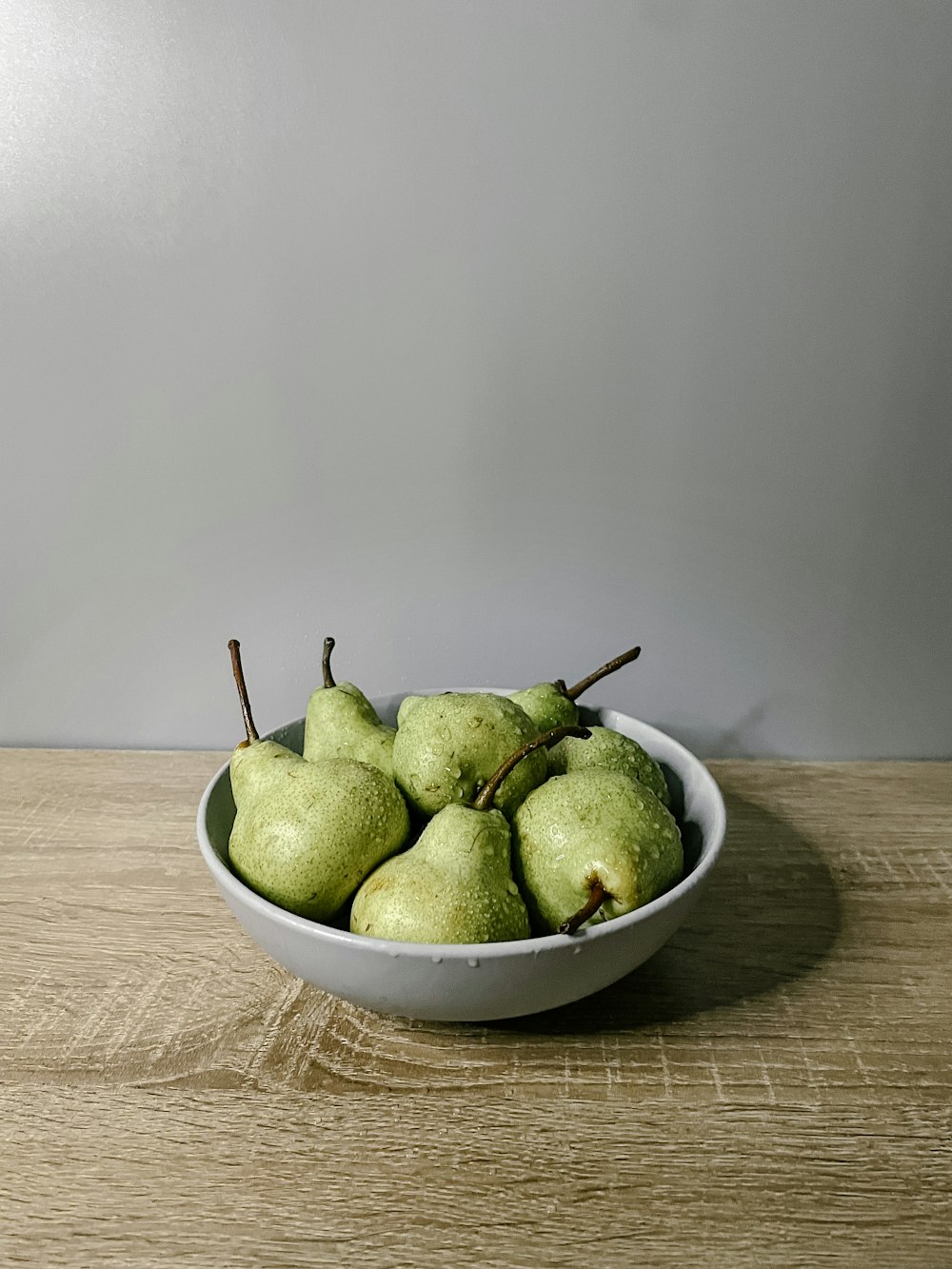 a bowl filled with green pears on top of a wooden table