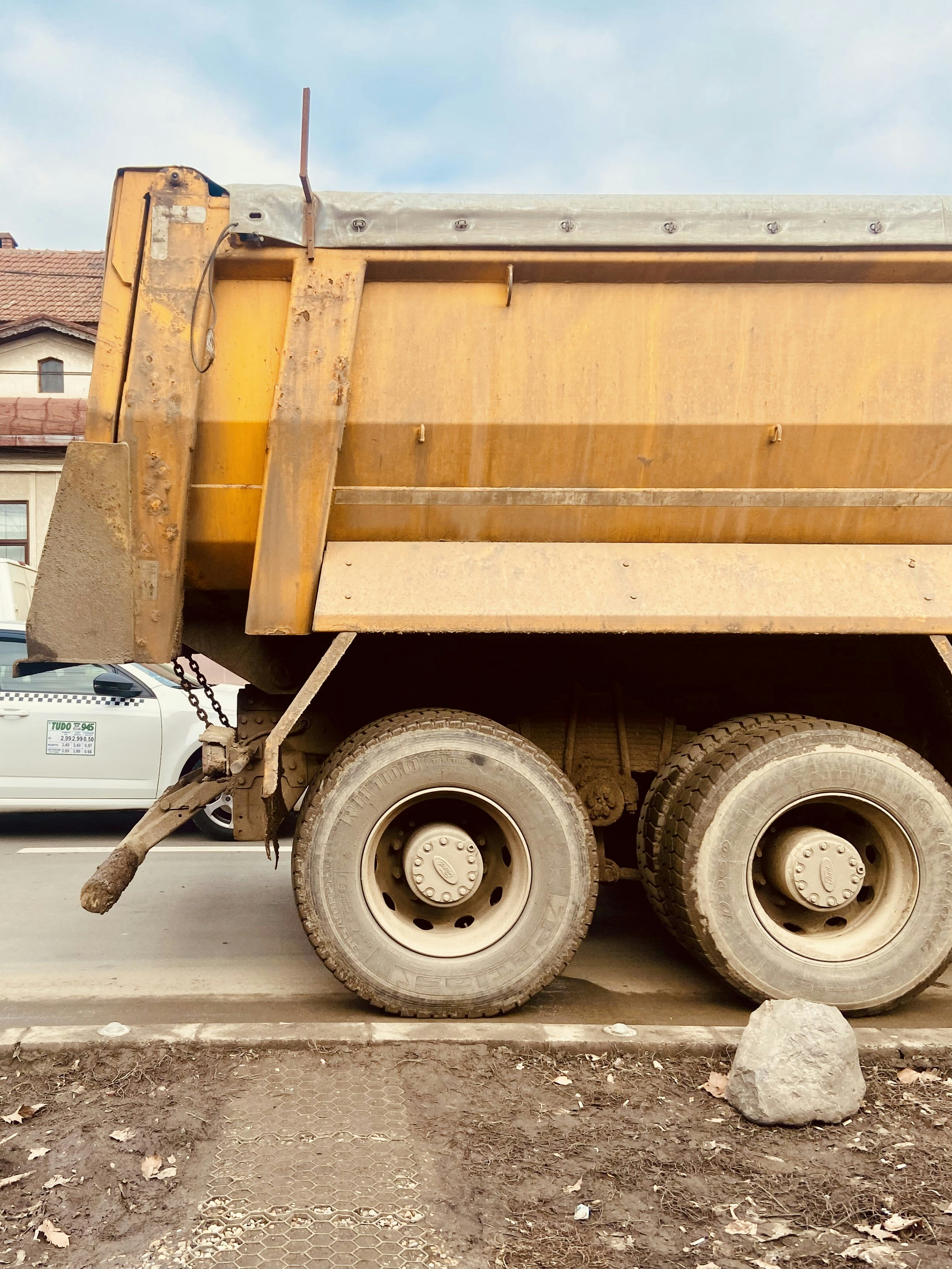 Big orange dump truck on a boulevard next to a construction site.