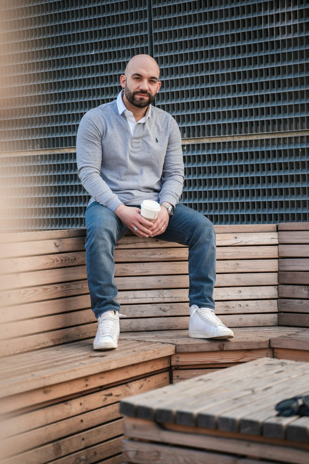 a man sitting on a wooden bench with a cup of coffee