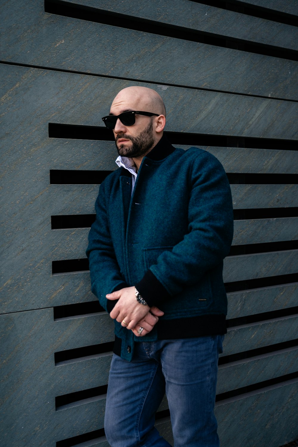 a bald man wearing sunglasses standing in front of a wall