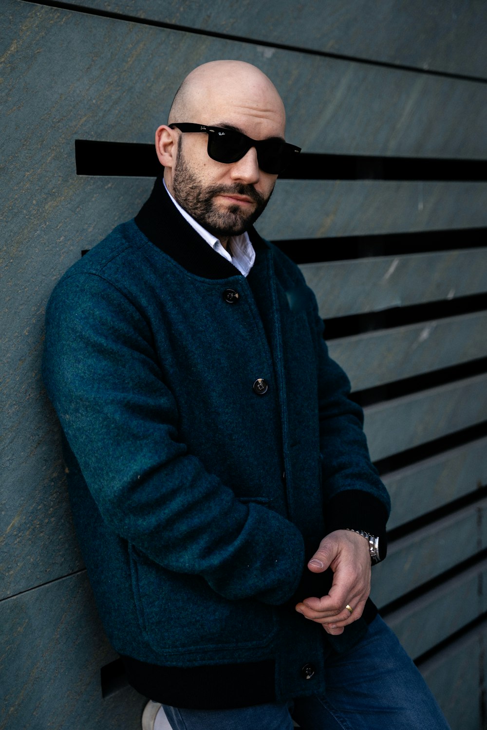 a bald man wearing sunglasses leaning against a wall