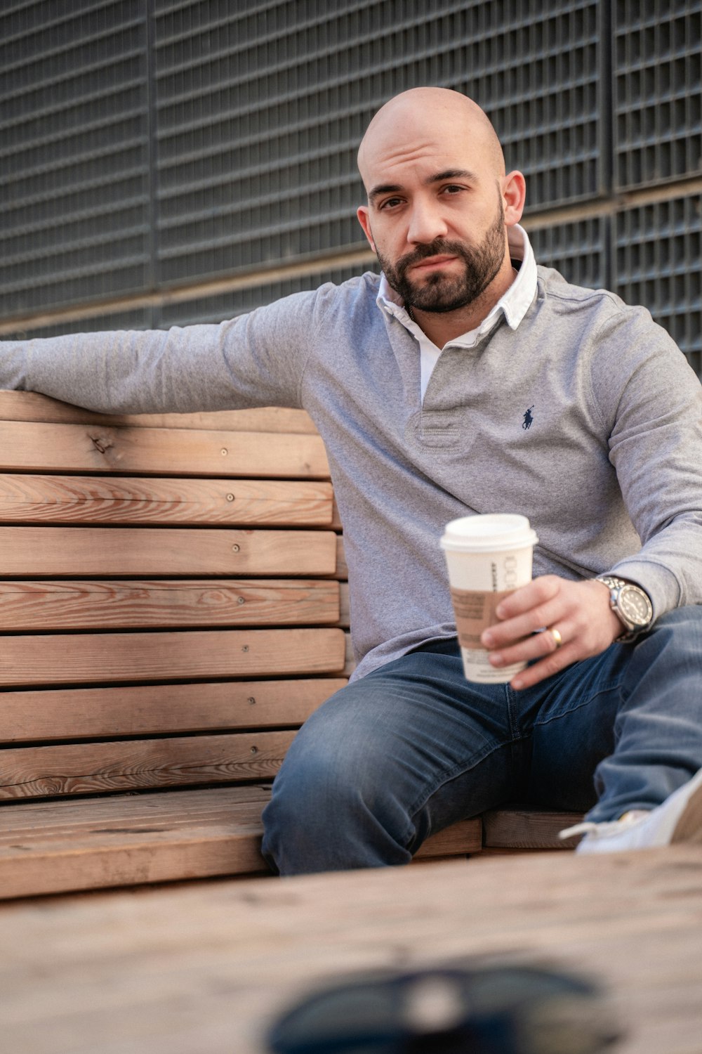 a man sitting on a wooden bench holding a cup of coffee