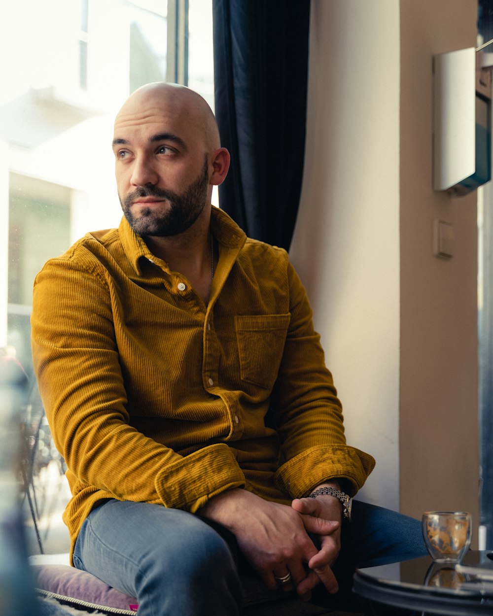 a bald man sitting on a chair in front of a window