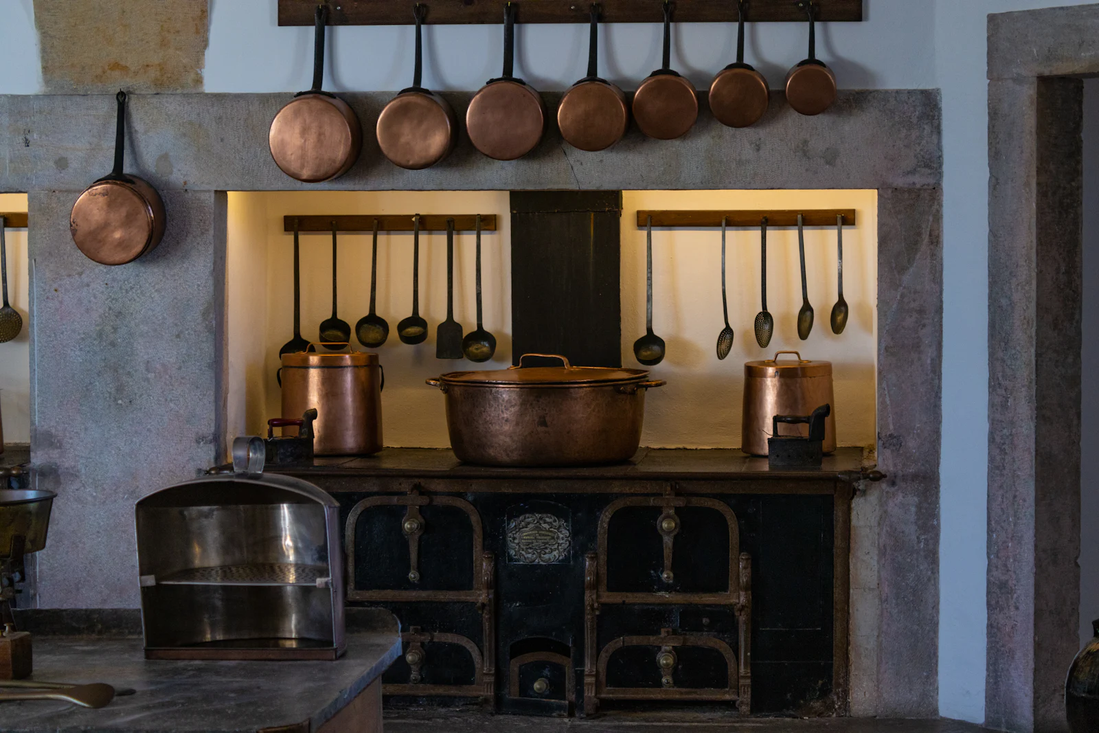 Copper pans and ladles hung above an old range in a warm kitchen.