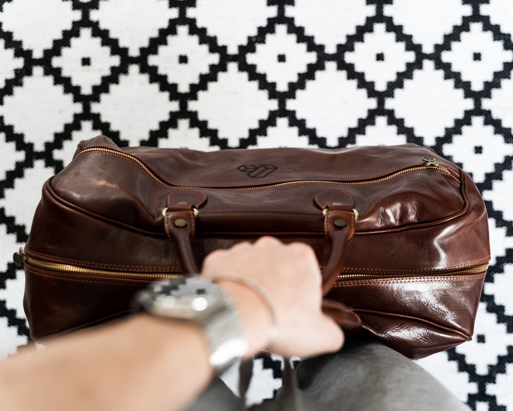 a person is holding a brown leather bag