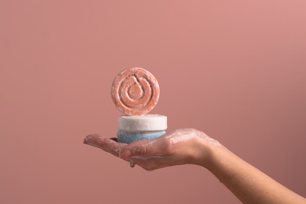 a hand holding a small cake with a spiral design on top of it