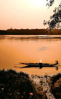 A peaceful river canoe gliding past lush green banks at sunset.