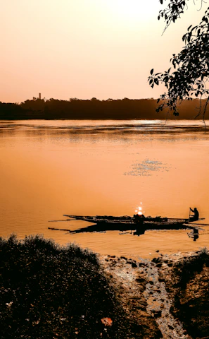 A peaceful river canoe gliding past lush green banks at sunset.