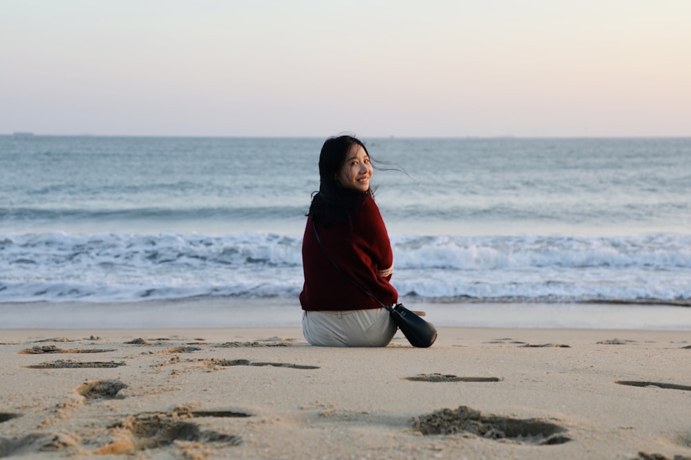 a woman sitting on the beach looking up at the sky