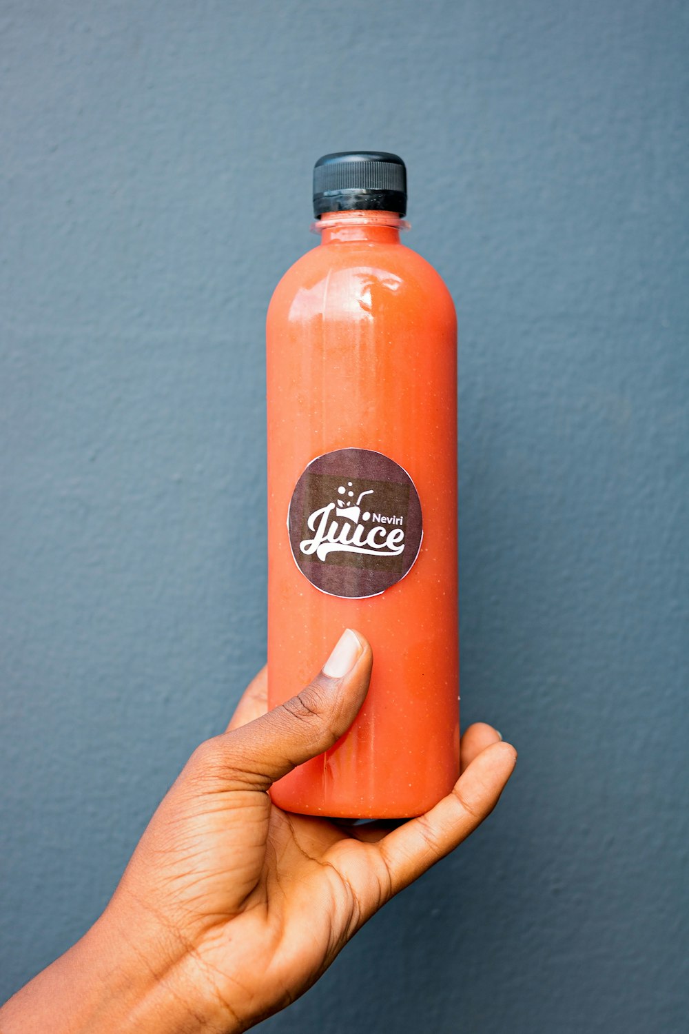 a hand holding an orange juice bottle in front of a blue wall