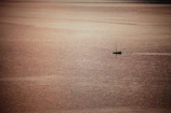 Wide-angle view of an open horizon with a solitary boat drifting under a sky painted in gold and charcoal.