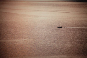 Wide-angle view of an open horizon with a solitary boat drifting under a sky painted in gold and charcoal.