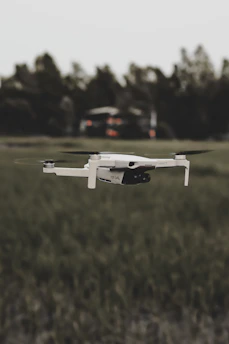 A sleek drone hovering over a sunlit field with a clear blue sky in the background.