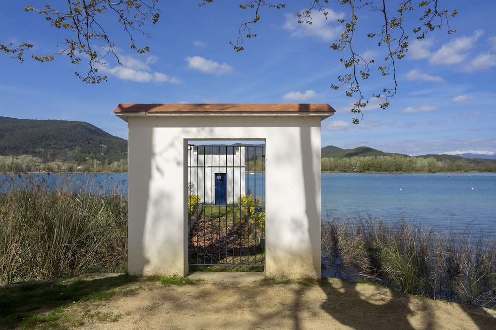 a small white building with a gate near a body of water