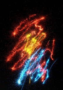 A colorful display of abstract, bright particles arranged in a chaotic yet visually pleasing pattern. The image features vibrant red, yellow, and blue streaks against a black background, resembling fireworks or energy bursts.