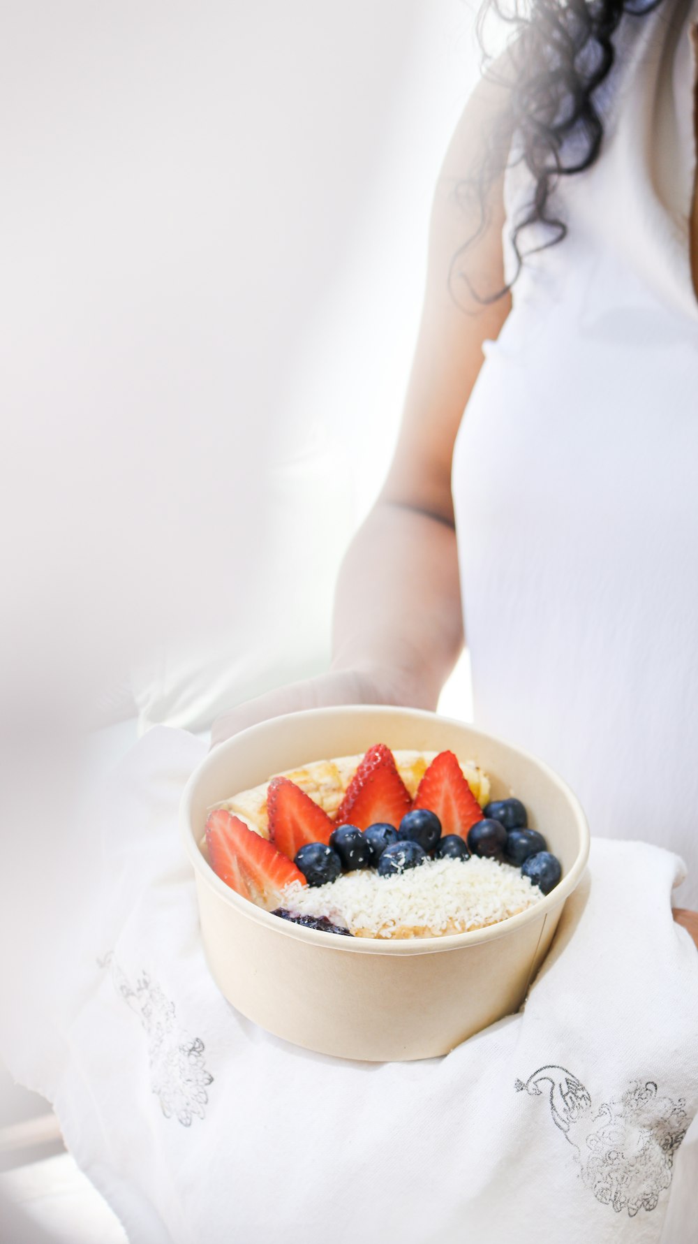 a woman is holding a bowl of cereal with strawberries and blueberries