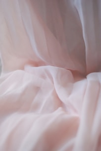 Soft, flowing fabric with delicate folds creates a gentle and airy texture. The material has a slightly sheer quality and a light, pastel pink hue.