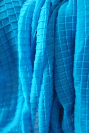 A close-up view of a textured fabric with a grid pattern. The fabric appears to be draped or folded, with visible shadows and highlights accentuating the three-dimensional quality of the material.