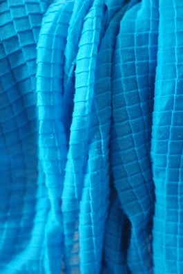 A close-up view of a textured fabric with a grid pattern. The fabric appears to be draped or folded, with visible shadows and highlights accentuating the three-dimensional quality of the material.