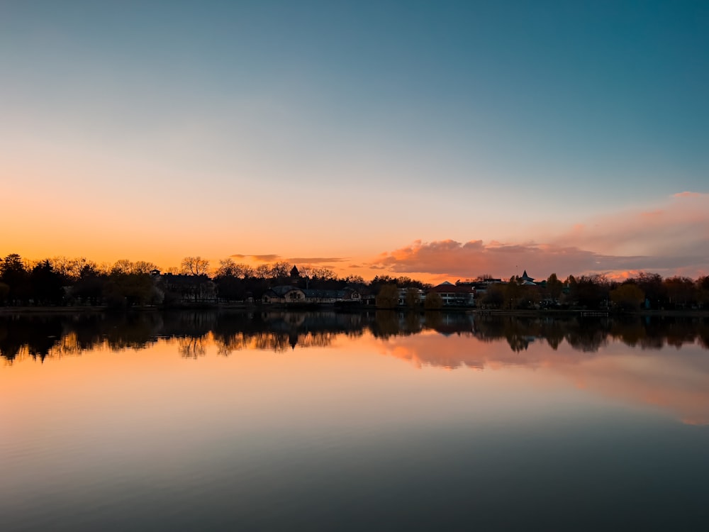 a body of water with trees and a sunset in the background