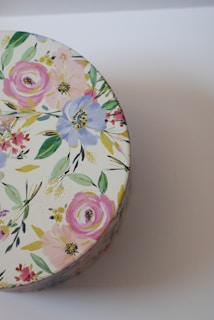 A round tin with a decorative floral pattern featuring pink, blue, and yellow flowers with green leaves on a light background.
