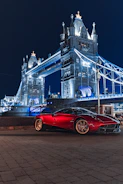 a red sports car parked in front of a large bridge at night