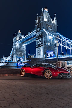 a red sports car parked in front of a large bridge at night